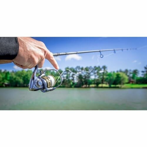 Close-up of a hand holding a fishing rod by a lake.